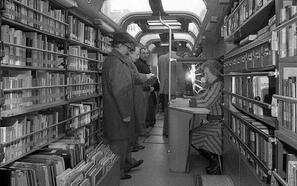 Die erste Generation des Medienbusses von innen. Auf dem schwarz-weiß Bild stehen Menschen vor den Regalen im Bus