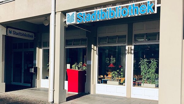 Der Eingang der Stadtteilbibliothek Waldstadt von vorne mit rotem Medienrückgabekasten.