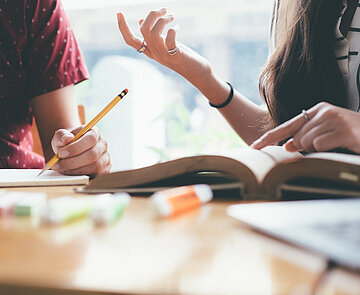 Zwei junge Leute sitzen an einem Tisch in einer Lernsituation.