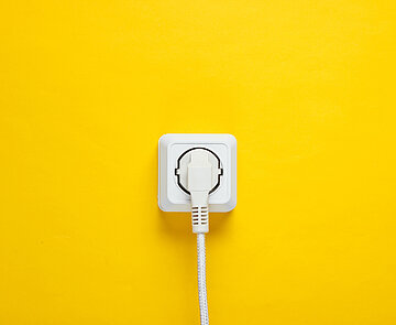Weißes Kabel in weiße Steckdose gesteckt an gelber Wand