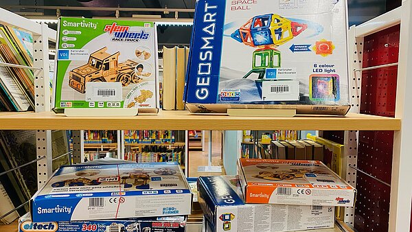 Ein Foto vom Regal in der Jugendbibliothek in dem gestapelt verschiedene Bau- und Experimentierkästen liegen, z.B. Geosmart und Gravitrax.