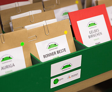 Nahaufnahme des verpackten Saatguts in Tütchen mit Beschriftung der Sorten in einer grünen Box