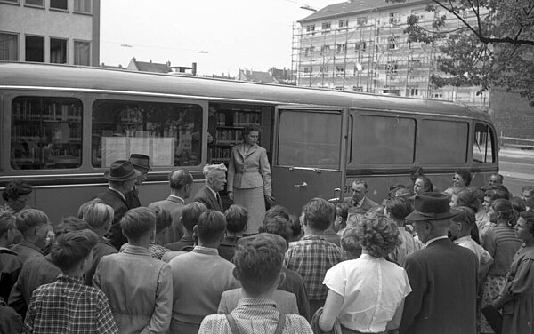 Eine Menschentraube vor der Autobücherei. In der geöffneten Tür steht eine Mitarbeiterin von damals