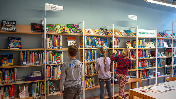 Drei Kinder stehen vor einem Bücherregal