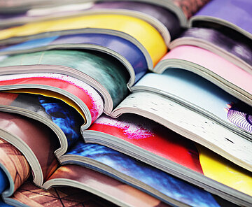 Eine Detailansicht von bunten Zeitschriften, die aufgeschlagen übereinander liegen.