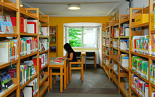 Eine Frau sitzt an einem Leseplatz, um sie herum viele volle Bücherregale