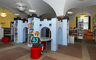 Die Ritterburg mitten in der Bibliothek, in der Kinder sitzen können. Vor der Ritterburg sitzt ein Junge auf einem Sitzsack