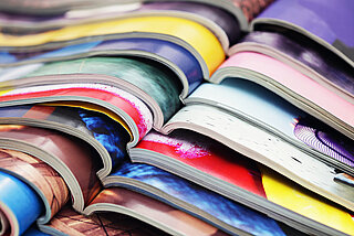 Eine Detailansicht von bunten Zeitschriften, die aufgeschlagen übereinander liegen.
