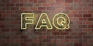 Die Neonleuchtbuchstaben F, A und Q vor an einer Backsteinmauer hängend