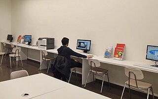 Ein Mann sitzt in unserem Lernstudio in Mühlburg am PC. Das ist ein großer Raum mit mehreren Computerarbeitsplätzen.