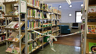 Das volle Bücherregal in dem die Saatgutbibliothek untergebracht ist, vorn mit einer Eröffnungsschleife versehen.