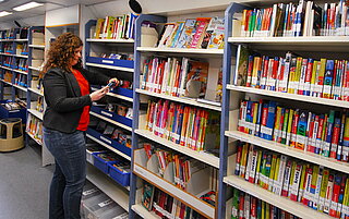Eine Mitarbeiterin steht vor den vollem Bücherregalen im Medienbus