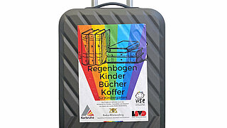 Der Regenbogenkinderbücherkoffer vor weißem Hintergrund. Ein Rollkoffer mit einem Rgeenbogenplakat drauf.